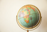 Vintage Mid Century Repologie Globe on a wooden stand, featuring muted blue oceans and colorful landmasses.