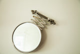 Circular beveled glass surface and polished silver-tone frame of the Deco shaving mirror.