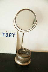 Slender aged metallic stand and perforated base of the antique shaving mirror.