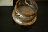 Vintage shaving mirror stand's tarnished metal brush holder with decorative perforated pattern.