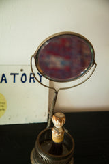 Angled view of a vintage shaving mirror with beveled glass and its brush in stand.