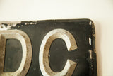 Distressed silver Art Deco D and C letters on black British license plate.