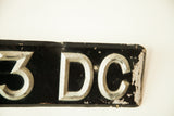 Aged silver Art Deco '3 DC' letters with chipped black paint on vintage British license plate.