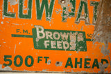 Chipped orange and rusty green 'Brown's Feeds' lettering on the antique metal sign.