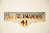 Hand painted Art Deco style Solimandos house sign with black and orange lettering, showing aged patina.