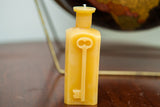 Yellow beeswax bottle candle with sloped shoulders and an embossed key.