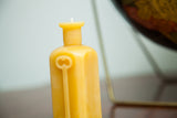 Natural yellow beeswax bottle candle with sloped shoulders and embossed skeleton key.