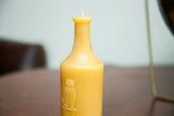 Light yellow beeswax candle shaped like an antique bottle with an embossed owl.