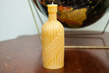 Yellow beeswax candle replicating an antique poison bottle with embossed text and grooves.