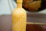 Close-up of golden beeswax candle bottle, highlighting embossed 'POISON' text and vertical grooves.