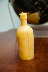 Amber-yellow beeswax candle, antique bottle shape, with prominent vertical grooves and embossed texture.