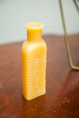 Yellow beeswax bottle candle with molded 'POISON' text and vertical ribbing.