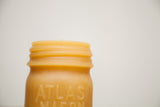 Embossed 'ATLAS MASON' lettering and threaded rim on a natural beeswax candle.
