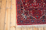 Vintage Bijar rug corner, with cherry red floral field, dark navy border, and white fringe.