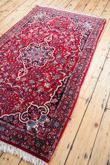 Cherry red Persian Bijar rug corner, with navy floral patterns and white fringe.