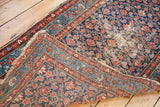Distressed blue Hamadan runner's folded corner, highlighting worn pile and brick red Herati motif.