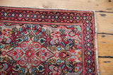 Persian Sarouk rug corner showing aqua and red floral patterns on creamy ivory, with patterned border.