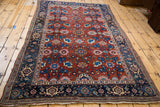 Angled view of a collector's antique Persian Bijar rug featuring a traditional red and blue Harshang pattern.