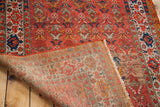 Antique Malayer rug folded back, displaying orange-red field, woven foundation, and natural fringe.