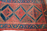 Antique Kurdish tribal rug detail: red geometric diamonds on deep blue, distinct red border.