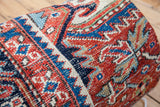 Worn hand-knotted Heriz rug detail, with geometric patterns in rust, sapphire blue, and cream.