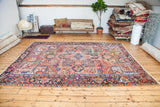Artfully worn Heriz rug corner, featuring faded reds, blues, geometric patterns, and fringe.