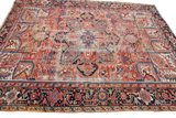 Distressed vintage Heriz rug corner with geometric patterns in rich reds and blues.