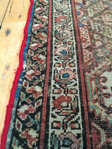 Distressed red edge, blue binding, and muted traditional patterns on the antique Northwest Persian rug.