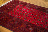 Deep cranberry red field with repeating Turkmen gul motifs and charcoal border.