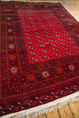 Vintage Turkmen Bokhara rug corner with cranberry red field, geometric border, and wool fringe.