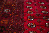 Vintage Bokhara rug featuring rich cranberry red geometric gul motifs and a detailed charcoal border.