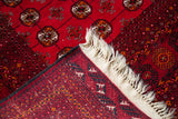 Vintage Bokhara rug corner: cranberry red pile, geometric guls, woven foundation, off-white fringe.