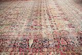 Distressed pile of an antique Persian Kerman rug, revealing faded cypress trees and restorative weaving.