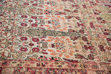 Detail of a Persian Kerman carpet's distressed surface, showcasing red and cream cypress tree motifs.