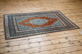 Angled view of an antique Haji Jalili Tabriz rug, showing its rust-orange field and aqua medallion.