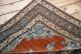 Intricate aqua blue corner spandrel and floral borders on a folded antique rust orange Tabriz rug.