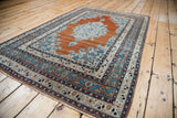 Antique Haji Jalili Tabriz rug shown at an angle, displaying its warm rust orange field and delicate blue details.