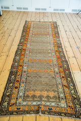 Distressed geometric border, time-softened orange motifs, and fringed end of antique runner.