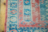 Distressed corner detail of vintage Turkish rug, featuring geometric patterns in raspberry red and aqua blue.