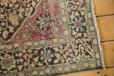Close view of the charcoal floral border, raspberry corner, and secured edge of an antique Persian rug.