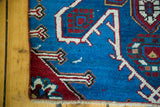 Antique Caucasian rug corner with expressive geometric red, blue, and white patterns.