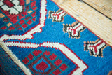 Textured close-up of unique red, blue, and white asymmetrical motifs on antique Caucasian rug.