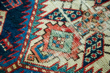 Intricate geometric motifs in time-softened red, blue, and teal on distressed antique Caucasian pile.