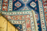 Antique Caucasian runner corner reveals hand-knotted tribal patterns, navy field, and original secured selvage.