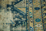 Geometric animal motifs and distressed indigo and gold textures on an antique Shirvan rug.