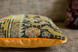 Textured edge of antique Caucasian fragment pillow; geometric orange, yellow, black patterns.