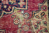 Distressed pile detail of an antique Kerman rug with blossoming red and beige florals.