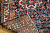 Vintage Persian rug corner showing dark blue field, rich floral motifs, and woven reverse.