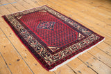 Vintage Serbend rug's cream border with scrolling vine motifs and cherry red field.
