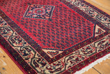 Corner of vintage Serbend rug, cherry red field with repeating Mir design and ornate tendril border.